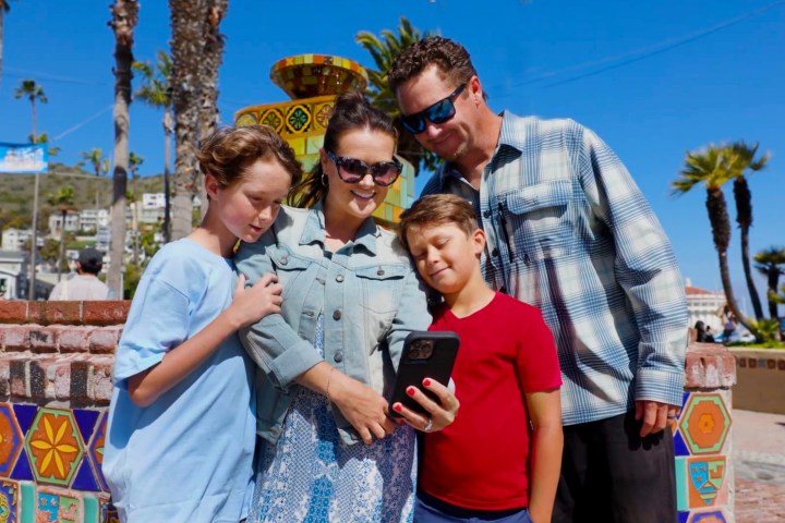 Family of four taking a selfie together near colorful tiles on a sunny day with palm trees in the background.