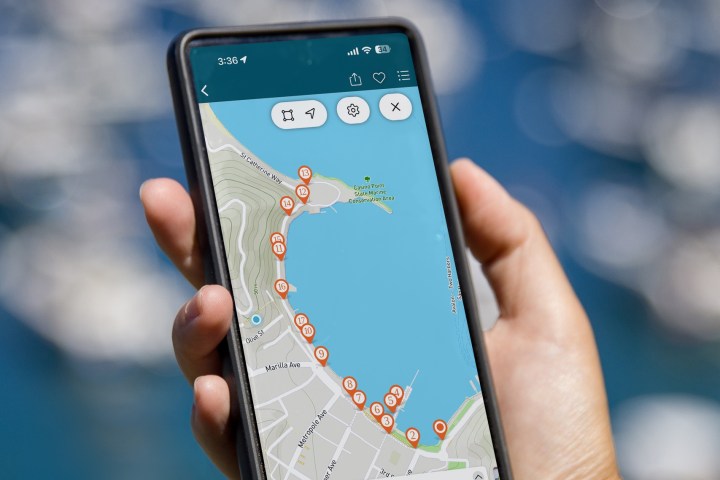 Hand holding a smartphone displaying a map with a coastal path and multiple marked locations.