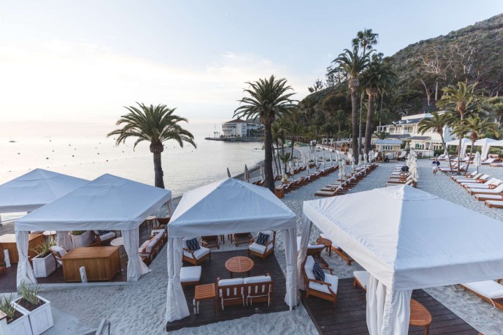 Beach with white cabanas, palm trees, and lounge chairs on sand near the ocean.