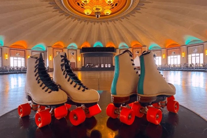 Pair of roller skates with red wheels on rink in ornate, domed room.