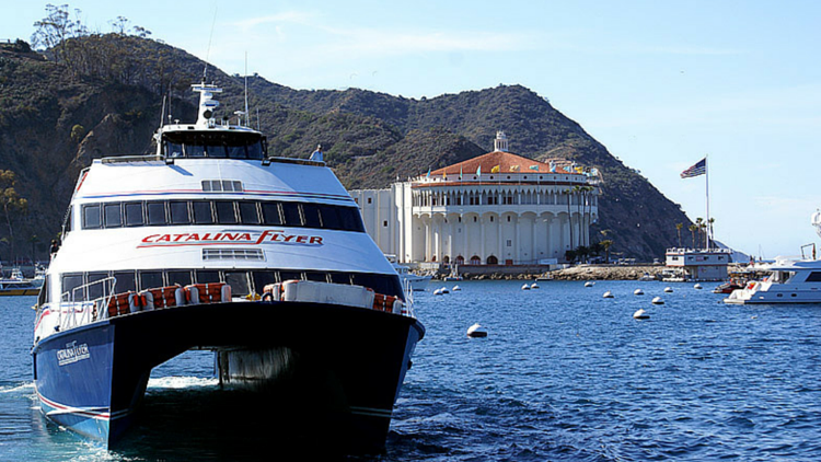 Boat named Catalina Flyer on water near a large white building with hills in the background.