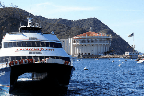 Boat named Catalina Flyer on water near a large white building with hills in the background.